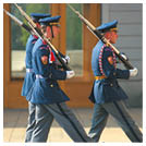 T i lid v uniform ch s  epicemi a b l mi rukavicemi nesou pu ky a pochoduj  synchronizovan  p ed budovou.  Popis generovan  AI