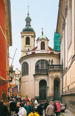  zk ulice s historickou architekturou a v    kostela v pozad  je pln  lid  v r zn m oble en , kte   proch zej  nebo stoj .  Popis generovan  AI