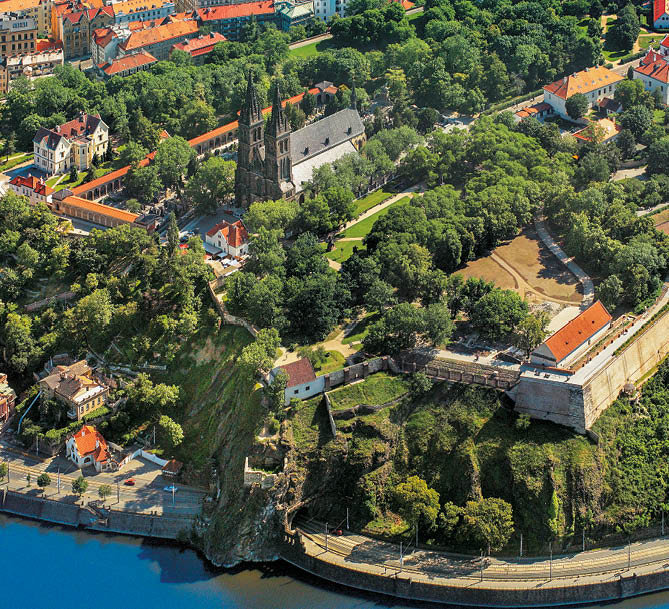 Leteck pohled na historickou   st m sta s kostelem, zelen mi parky, star mi budovami a  ekou v pop ed .  Popis generovan  AI