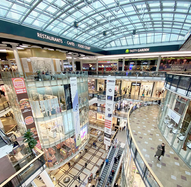 Modern n kupn  centrum s prosklenou st echou, n kolika patry, eskal tory a lidmi proch zej c mi kolem obchod  a restaurac .  Popis generovan  AI