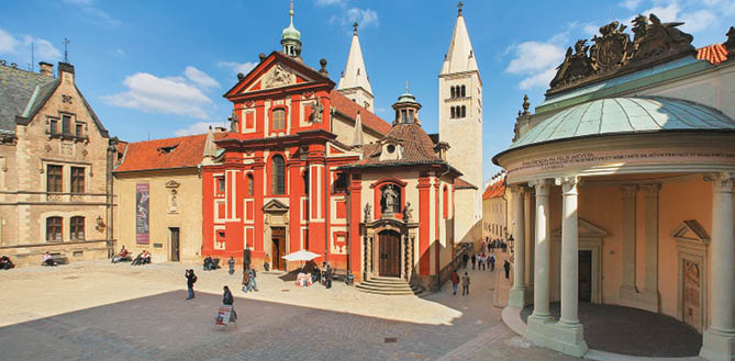 N m st s historick mi budovami v etn   erven  barokn  kaple a lidmi proch zej c mi kolem za slune n ho dne.  Popis generovan  AI