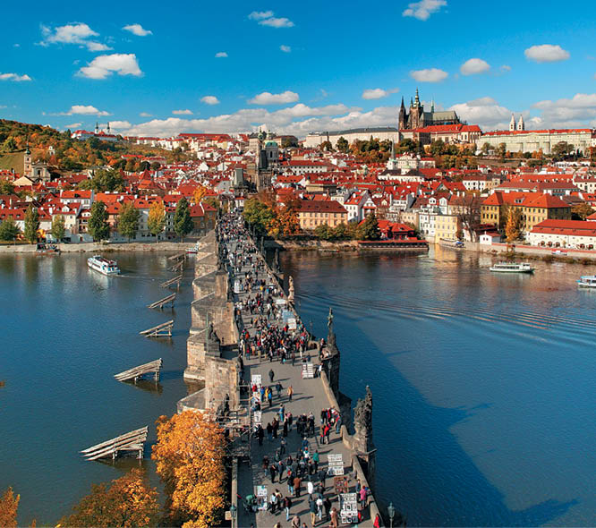 Starobyl most pln  lid  vede p es  eku k historick mu m stu s  erven mi st echami a velk m hradem na kopci za jasn ho dne.  Popis generovan  AI
