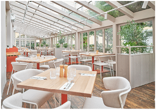 Restaurace s d ev n mi stoly a idlemi v prosklen  m stnosti s v hledem do zahrady.  Popis generovan  AI