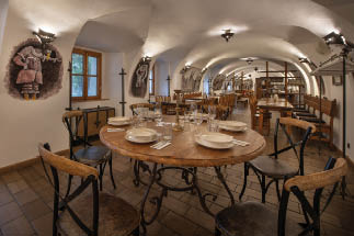V historicky za zen  restauraci s klenut mi stropy je d ev n  st l p ipraven  na j dlo s tal  i, sklenicemi a p  bory a kolem n j jsou  idle.  Popis generovan  AI
