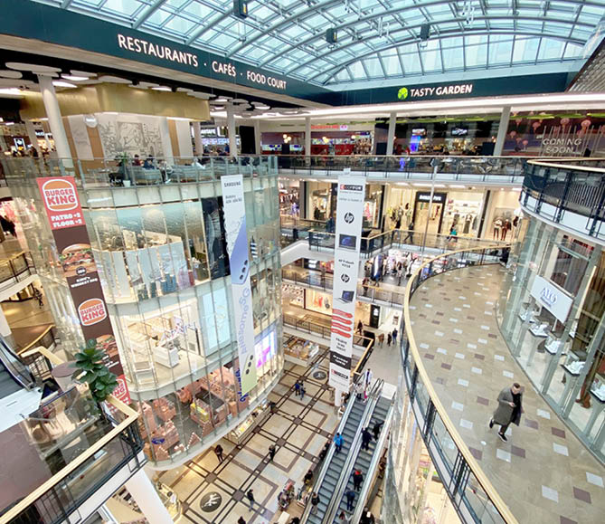 Modern n kupn  centrum s n kolika patry, eskal tory, restauracemi a lidmi proch zej c mi se po chodb ch.  Popis generovan  AI