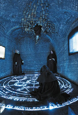 T i osoby v tmav ch pl t ch stoj  a kle   v m stnosti s modr m osv tlen m a magick mi symboly na podlaze a strop , kde jedna osoba vis  hlavou dol .  Popis generovan  AI