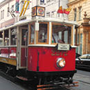  erven historick  tramvajov  v z s   slem 2272 jede po kolej ch v m stsk  ulici s budovami v pozad .  Popis generovan  AI