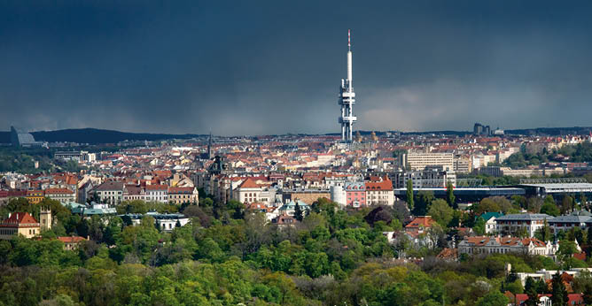 Panoramatick pohled na m sto s v raznou televizn  v    uprost ed a zelen mi stromy v pop ed  pod zata enou oblohou.  Popis generovan  AI